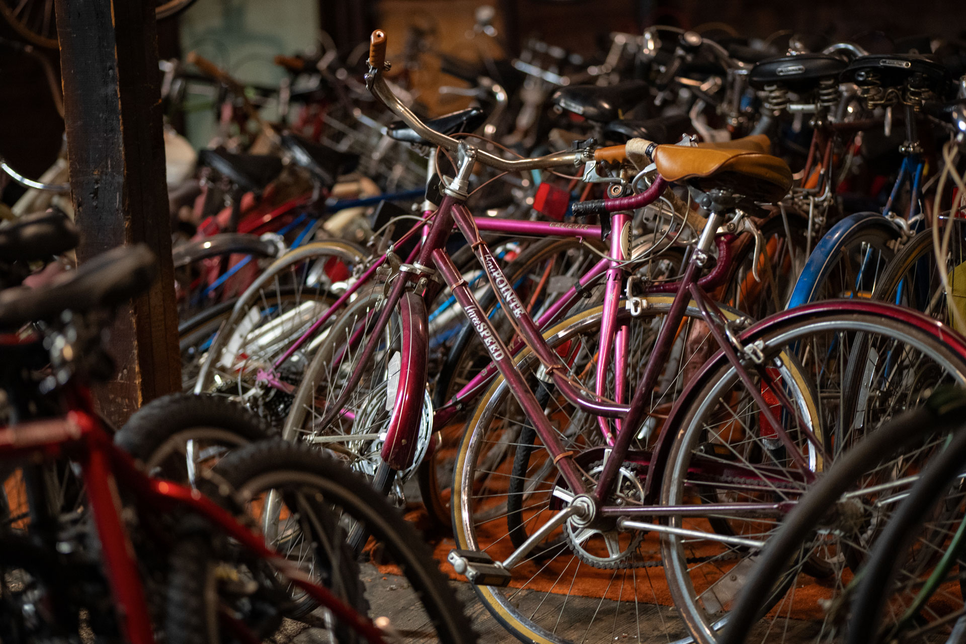 A maroon bicycle stands out amongst a large pile of bicycles.